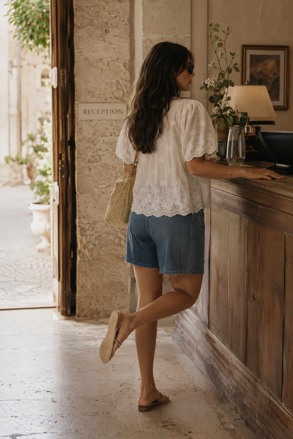 Vista trasera de blusa blanca bordada con mangas cortas festoneadas, llevada con bermuda denim y bolso de fibras naturales en un estilismo casual chic mujer | STRANNA