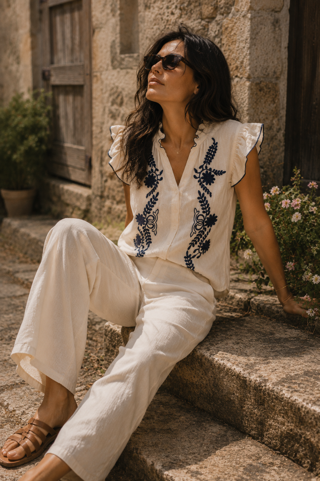 Blusa crema con bordados azul marino y volantes en los hombros, combinada con pantalón fluido y gafas de sol en un look casual chic | STRANNA
