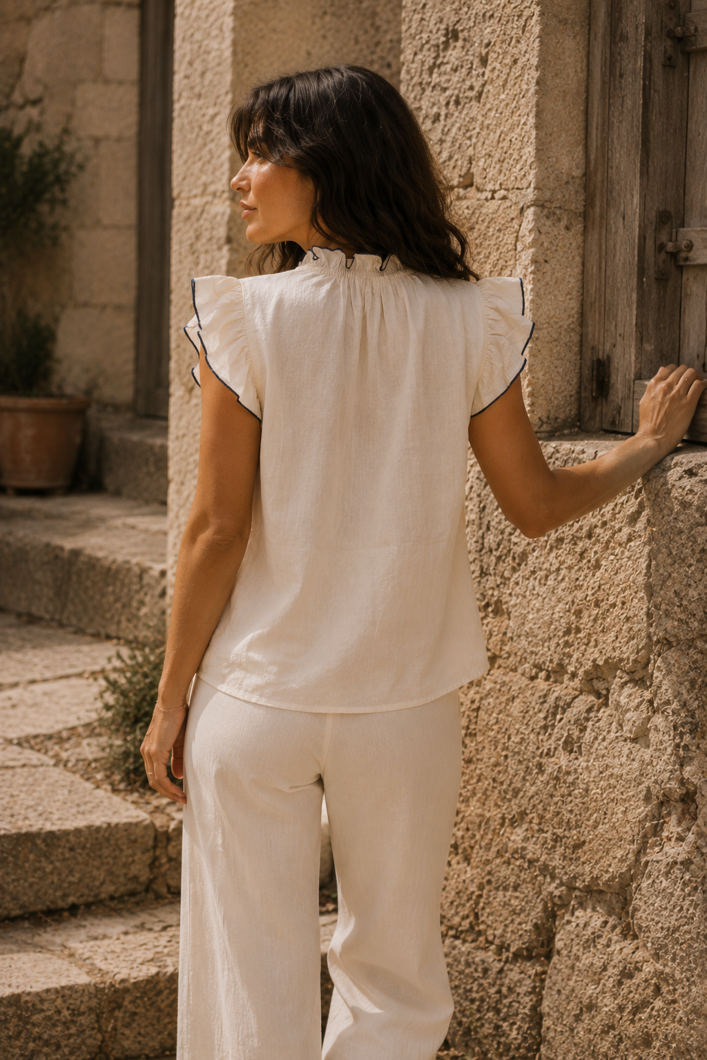 Vista trasera de blusa crema de algodón con cuello fruncido y mangas de volante ribeteadas, combinada con pantalón blanco | STRANNA